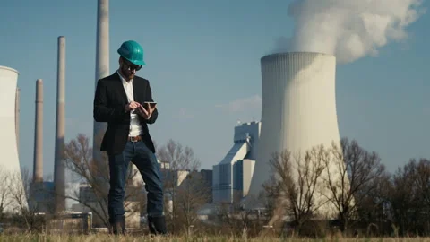 Electric engineer wearing helmet and suit in front of coal fired power station Stock Footage 209349904