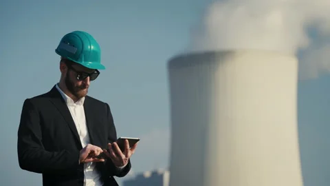 Electric engineer wearing helmet and suit in front of coal fired power station Stock Footage 209350499