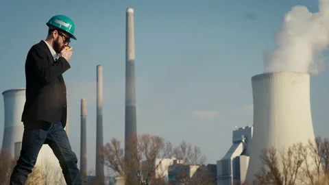 Electric engineer wearing helmet and suit in front of coal fired power station Stock Footage 209353436