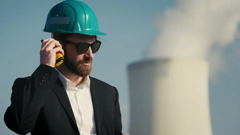 Electric engineer wearing helmet and suit in front of coal fired power station Stock Footage 209357182
