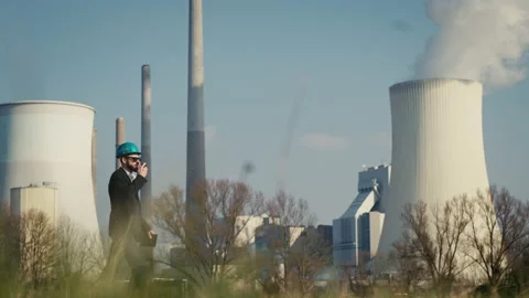 Electric engineer wearing helmet and suit in front of coal fired power station Stock Footage 209358987