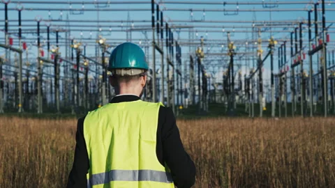 Electric engineer wearing helmet suit and safety vest walking towards substation Stock Footage 171190413