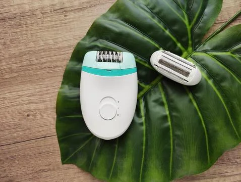 Electric epilator with interchangeable shaver head on a green tropical leaf Stock Photos