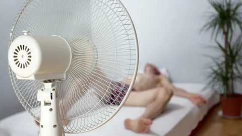An electric fan cools a man lying in a room in the summer heat. Stock Footage 160271491