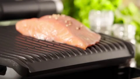 Electric grill on kitchen table, putting salmon fish defocused. Food preparation Stock Footage 223597643