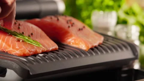 Electric grill on kitchen table, putting second part salmon fish on grill Stock Footage 223762472