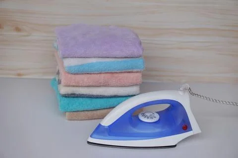 Electric iron and stack of folded clothes Stock Photos