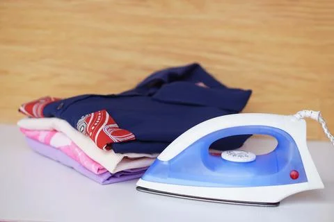 Electric iron and stack of folded clothes Stock Photos