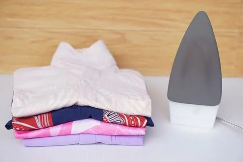 Electric iron and stack of folded clothes on table. Concept, daily chore, househ Stock Photos