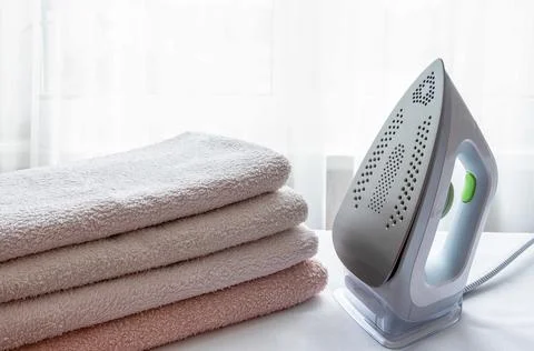 An electric iron and a stack of ironed towels on a light surface Stock Photos