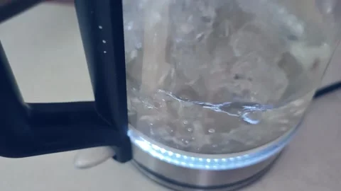 Electric kettle boiling water with visible bubbles and steam rising, showcasing Stock Footage 334324372