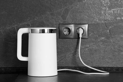 Electric kettle plugged into power socket on dark grey wall indoors Stock Photos
