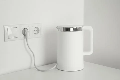 Electric kettle plugged into power socket on white wall Stock Photos