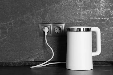Electric kettle plugged into power socket on dark grey wall indoors Stock Photos