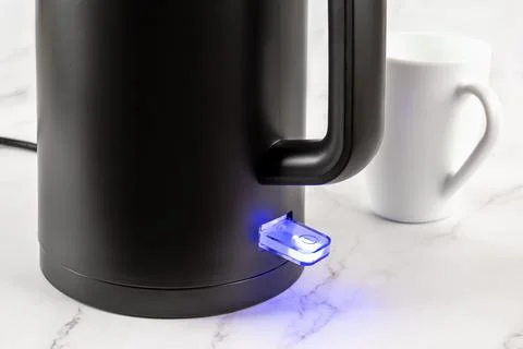Electric kettle switch glows blue while turned on. Matte black kettle. Stock Photos