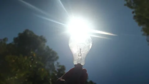 Electric light bulb held by a person's hand silhouette in the sun Stock Footage 240462090