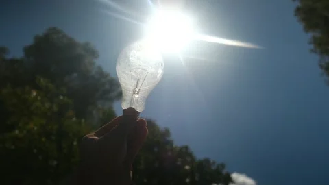 Electric light bulb held by a person's hand silhouette in the sun Stock Footage 240462093