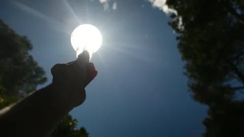 Electric light bulb held by a person's hand silhouette in the sun Stock Footage 240462099