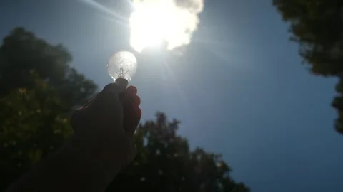 Electric light bulb held by a person's hand silhouette in the sun Stock Footage 240462112