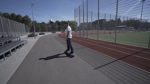 Electric Longboard man in white t-shirt and hat ride on red sport stadium with Stock-Footage 90813870