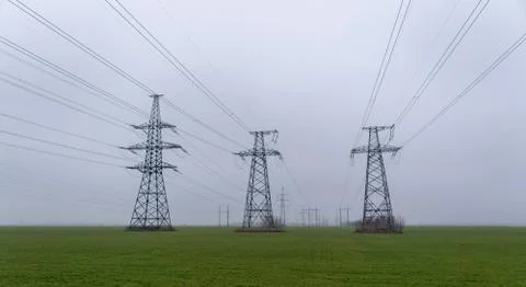 Electric network of pylons against a cloudy sky and a green meadow Fotos de archivo