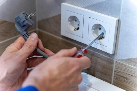 Electric plug is being inserted into a wall socket with a screwdriver nearby Stock Photos