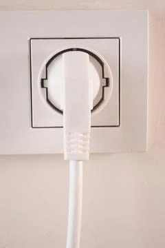 Electric plug inserted into a wall socket in indoor setting Stock Photos
