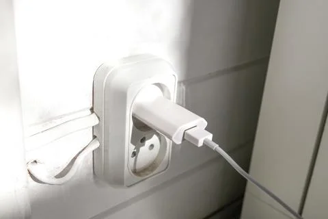 An electric plug inserted in a white socket on the wall Stock Photos
