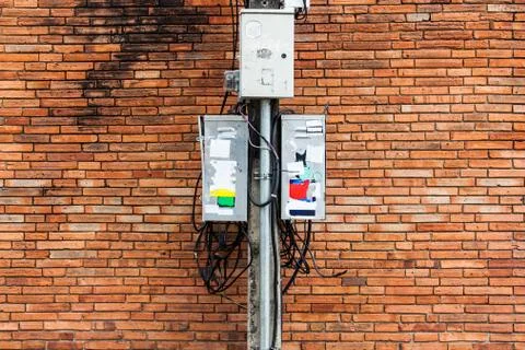 Electric pole with dirty electrical control box and cable, brick wall backgro Stock Photos