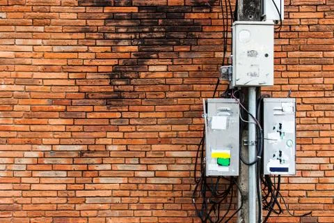 Electric pole with dirty electrical control box and cable, brick wall backgro Stock Photos