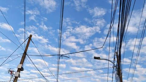 Electric poles with a complex network of cables under a cloudy blue sky Fotos de archivo