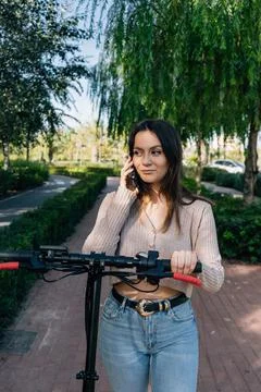 Electric scooter and mobile device. Girl calling on her smartphone while walk Stock Photos