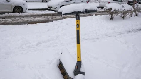 An electric scooter, covered in a layer of snow, is captured on a snowy street. Stock Footage 325180337