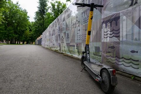 Electric scooter rests beside a long, patterned fence. Trees line the pathway 写真素材