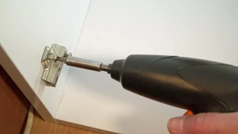 Electric screwdriver mounting a metal hinge on a white cabinet concept of D.. Stock Footage 330976376