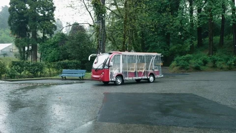 Electric shuttle bus parked in rainy weather at lush, green park, showcasing Stock Footage 274681237