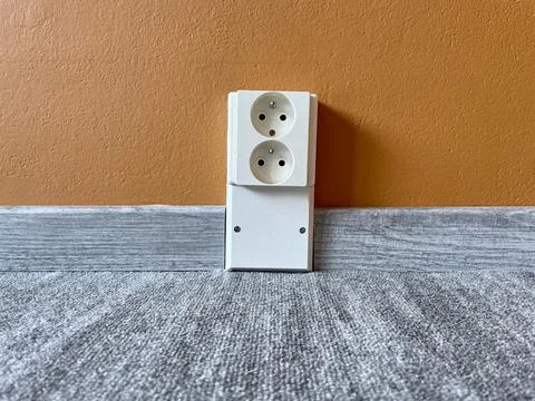 Electric socket by the floor between plastic baseboard with a wooden texture Stock Photos