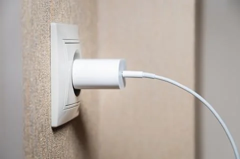 Electric socket on a pink wall. The black wire plug is connected. Renovated Stock Photos