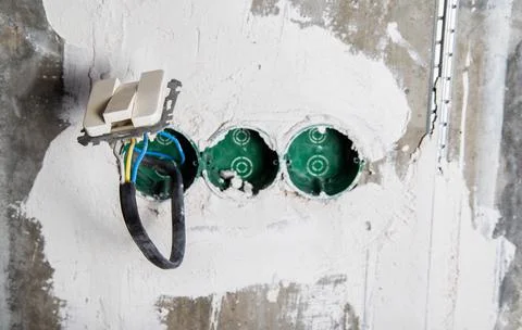 An electric switch hangs on wires from socket boxes built into a concrete wall Foto stock