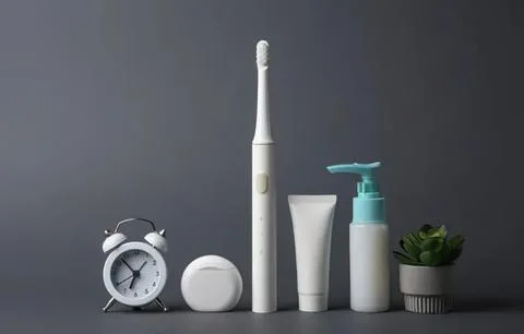 Electric toothbrush with clock, toothpaste, and plant on gray background Fotos de archivo