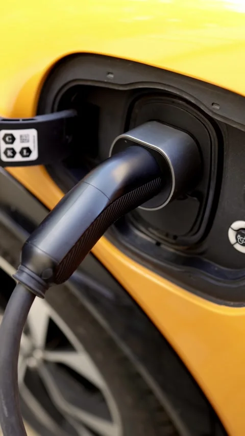 Electric vehicle charging cable connected to a yellow car, showcasing the Stock Footage 337386171