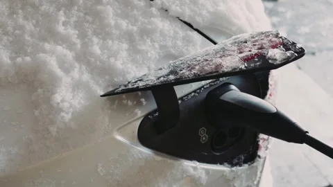 Electric vehicle charging cable plugged into white car covered in snow in winter Vídeo Stock 329632660