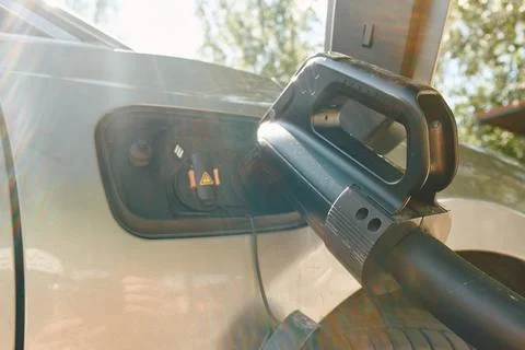 Electric vehicle charging plug inserted into car charging port with sun flare Photos