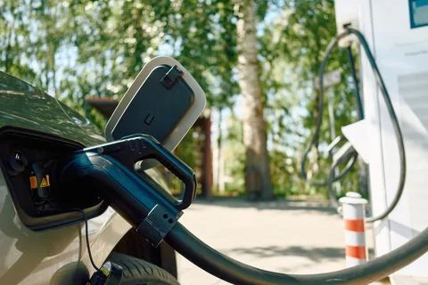 Electric vehicle charging plug inserted into car charging port with sun flare Stock Photos