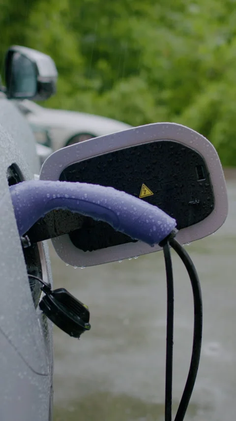 Electric vehicle charging process with close-up of charging connector, rain 库存影片 337996136