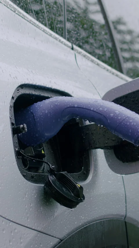 Electric vehicle charging process in the rain with a close-up view of the Stock Footage 340325810