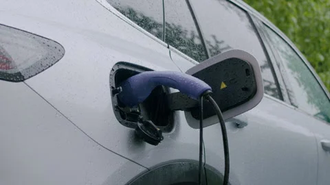 Electric vehicle charging in the rain with a close-up view of the charging port Stock Footage 337996477