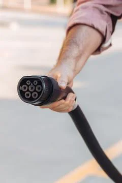 Electric vehicle or EV car socket held by a hand in a charging station. Elect Stock Photos