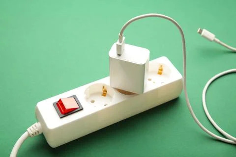 Electric white portable socket with connected device on green background. Stock Photos