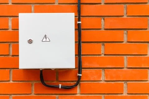 Electrical box with cable and danger sign on a red brick wall. Stock Photos